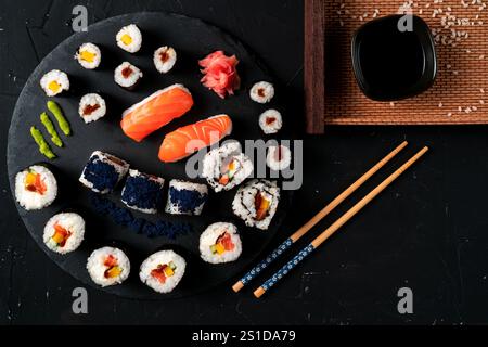 Sushi board with soy sauce and chopsticks. Japanese food on black plate and black background. A typical Japanese meal. Stock Photo