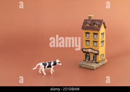 Miniature house building model with cow on brown background Stock Photo