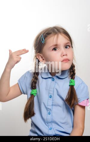 A portrait of a young girl with long brown braids, wearing a light blue shirt. She's making a playful hand gesture near her head. Stock Photo