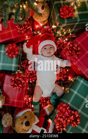 baby in santa hat on a blanket under christmas tree with gifts bows Stock Photo