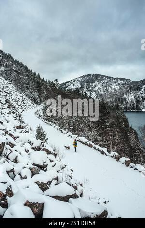 Hiker walks dog along snow covered trail in Acadia in winter Stock Photo