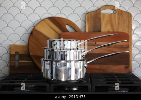 Stacked saucepans on stove with wooden boards in the background Stock Photo