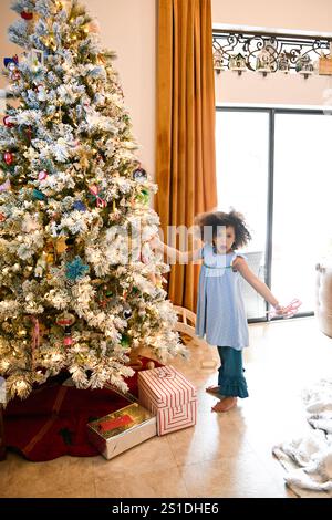 Child in blue dress near decorated Christmas tree with presents. Stock Photo