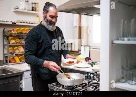 Professional chef is preparing meal in restaurant's kitchen. He makes a vegetarian lunch. He is adding spices. Stock Photo