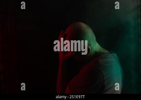 White, bald and bearded man, head down. Studio portrait with black background and colored lights. South American person. Stock Photo