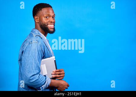 Young man holding tablet and looking over shoulder, smiling on a blue background, ready for his online class Stock Photo