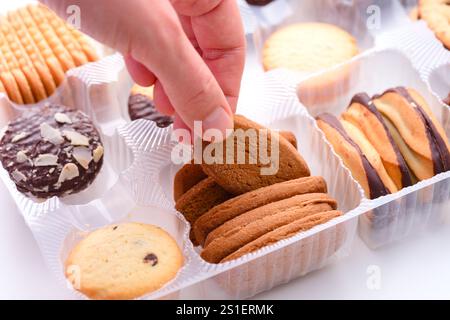 Woman hand taking cookie from plastic box with different kinds of cookies in it. Close-up Stock Photo