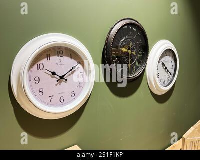 Kyiv, Ukraine - January 03, 2025: A collection of three clocks featuring distinct designs, mounted on a green wall. Showcases modern and vintage aesth Stock Photo