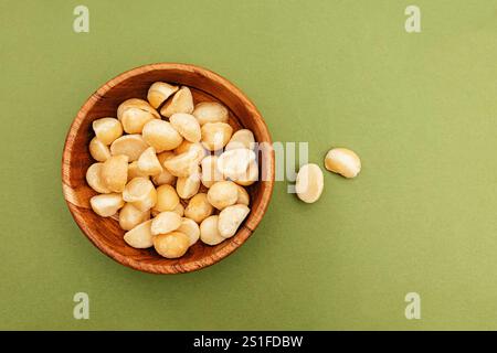 Wooden bowl filled with macadamia nuts on green background, top view Stock Photo