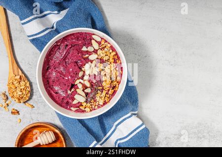 Berry smoothie bowl topped with granola and almonds served on a blue kitchen towel Stock Photo