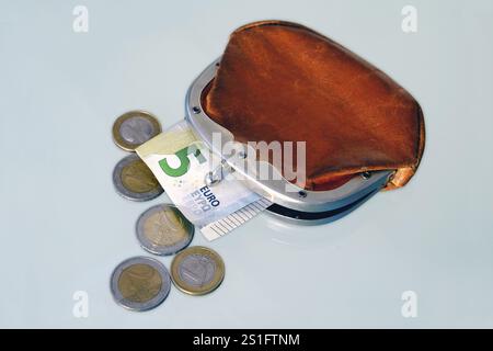 Slightly opened old-fashioned purse made of brown leather, with a five-euro note sticking out of it and five individual coins lying in front of it. Cu Stock Photo