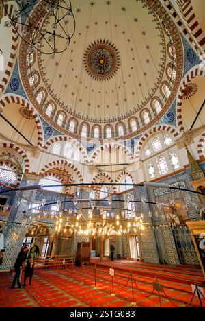 Rustem Pasha Mosque Dome Iznik Tiles Istanbul | ISTANBUL, Turkey — A wide-angle view captures the painted dome and tiled arches of the Rustem Pasha Mosque's prayer hall, where a central sunburst medallion crowns the octagonal ceiling above a ring of hanging lamps. The dome spans roughly 50 feet (15.2 m), among the largest Mimar Sinan built for a grand vizier in the Ottoman capital. Stock Photo