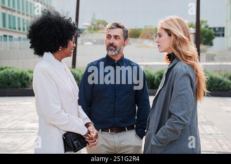 Three professionals engaged in discussion outdoors showcasing collaboration and communication. Group of business people talking together in a office break. Corporate workers having a discussion. High quality photo Stock Photo