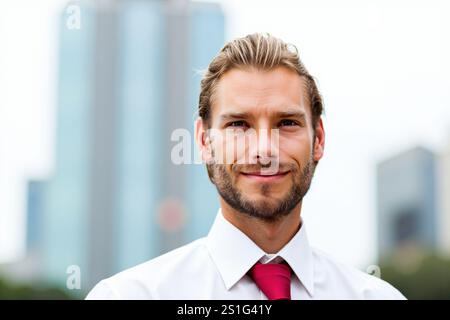Portrait of a young, successful businessman smiling confidently in front of a modern city skyline, conveying professionalism and success in the corpor Stock Photo