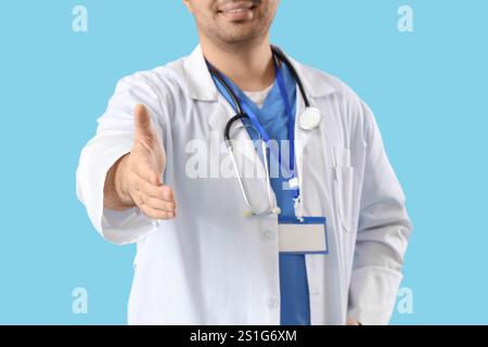 Male doctor offering hand for handshake on blue background, closeup Stock Photo