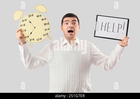 Stressed young man holding clipboard with word HELP and paper alarm clock on light background. Time management concept Stock Photo