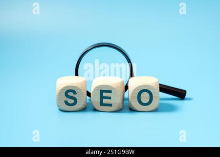 SEO, Search Engine Optimization text wooden cube blocks with a magnifying glass on blue background, idea of strategy, advertising, marketing, keyword and content concept Stock Photo