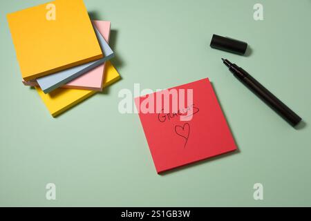 Red sticky note with "Gracias" and heart drawing on pastel background Stock Photo