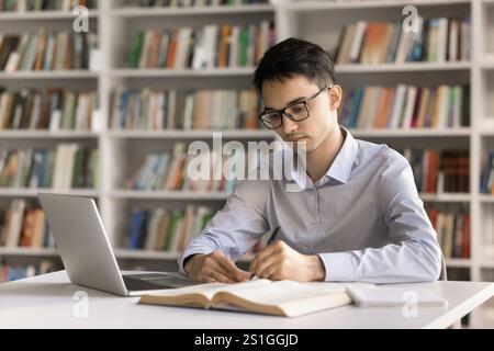 Serious motivated young male student taking notes at library desk Stock Photo