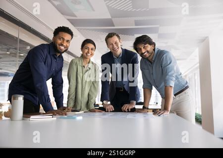 Multiethnic team of ambitious young colleagues standing at workplace Stock Photo