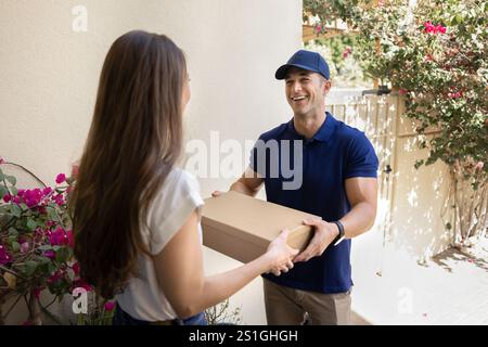 Happy courier in blue uniform cap giving parcel to client Stock Photo