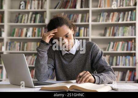 Serious young guy student engaged in reading book at library Stock Photo