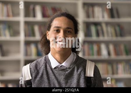 Headshot smiling teen guy student standing in library with backpack Stock Photo