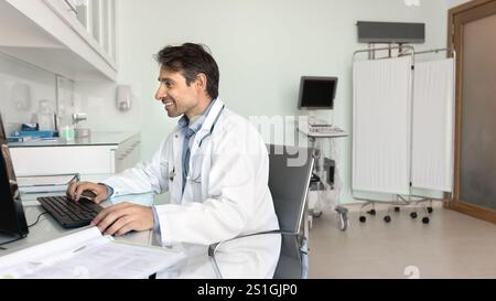 Happy middle aged Hispanic doctor man using desktop computer Stock Photo