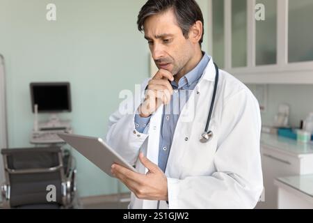 Concerned anxious senior Latin doctor man reading electronic medical report Stock Photo