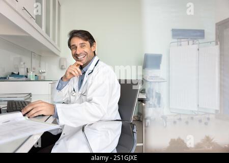 Portrait of happy successful male doctor sitting at workplace table Stock Photo