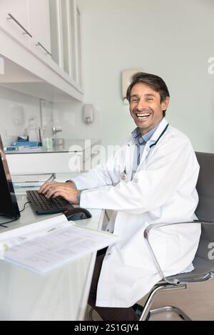 Happy successful Hispanic practitioner man working at desktop Stock Photo