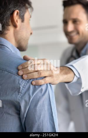 Hand of positive young male doctor touching shoulder of patient Stock Photo