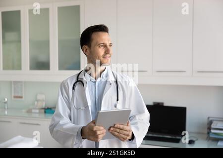 Positive pensive young doctor man holding tablet Stock Photo