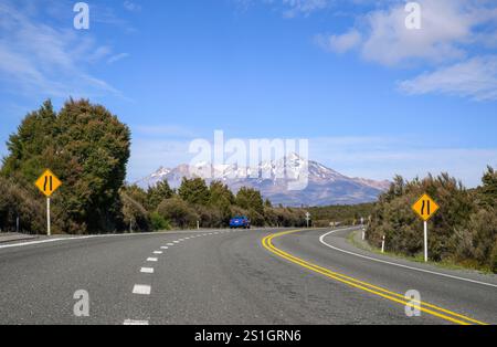 Road narrows on left road sign on Desert road. Mount Ruapehu in the distance. New Zealand. Stock Photo