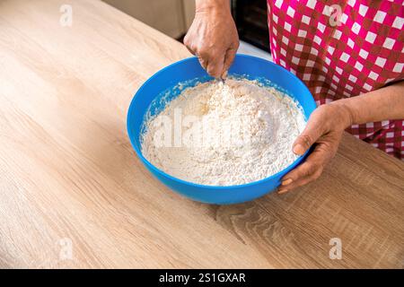 Woman stirs around spoon in bowl flour. Woman kneading dough by hand yeast dough. Woman hands and dough in a blue metal bowl. Female chef preparing Stock Photo