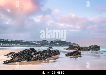 Pastel coloured sky over rocks exposed by a low tide on Gt Western Beach on the coast of Newquay in Cornwall in the UK. Stock Photo