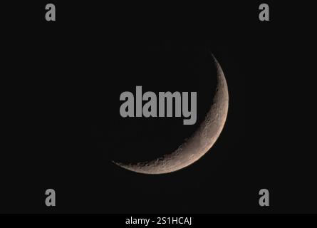 A close-up view of a crescent moon showcasing detailed craters and textures against a dark night sky Stock Photo
