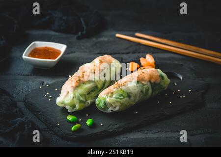 Two summer rolls with salad and salmon on black background, japanese, asian food Stock Photo