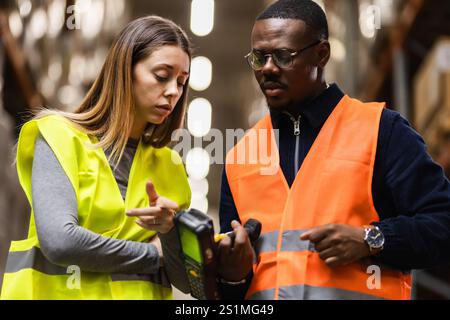 Focused warehouse workers in safety vests collaborate using a handheld device. The team discusses logistics operations and data management within an i Stock Photo