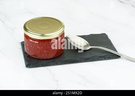 A closed glass jar with red caviar and a spoon on a mica serving board. Copy space. Stock Photo