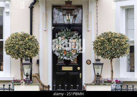 Fancy Christmas wreath hanging on the door of a large white house, England, UK, with topiary standards on either side Stock Photo