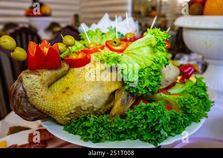 A beautifully arranged festive dish showcases a roasted duck adorned with fresh vegetables like lettuce, tomatoes, and olives. This culinary masterpie Stock Photo