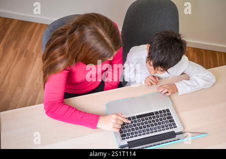 Babysitter pointing at laptop keyboard, helping a child with homework, seen from above Stock Photo
