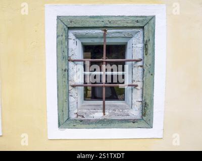 Old window with rusty metal bars reflecting photographer on yellow wall of ancient building Stock Photo