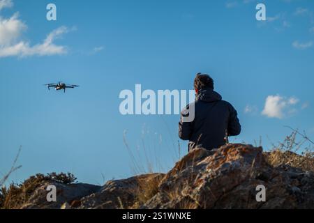 Man controlling drone with remote in nature with clear sky and rocky surroundings. The setting shows a sense of technology and exploration Stock Photo