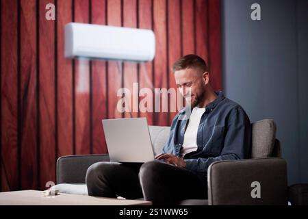 Happy Young Man Holding Remote Control Relaxing Under The Air Conditioner Stock Photo