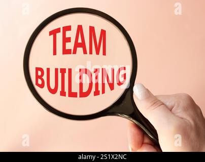 Team Building symbol. Concept word Team Building on magnifying glass. Businessman hand. Beautiful pink background. Business and Team Building concept. Stock Photo