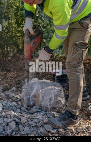 A worker smashes a large concrete block using an electric demolition hammer Stock Photo