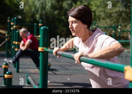Mature woman doing push-ups from the crossbar on outdoor sports ground Stock Photo