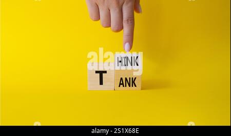 Think Tank symbol. Businessman hand points at turned wooden cubes with words Think Tank. Beautiful yellow background. Business and Think Tank concept. Stock Photo